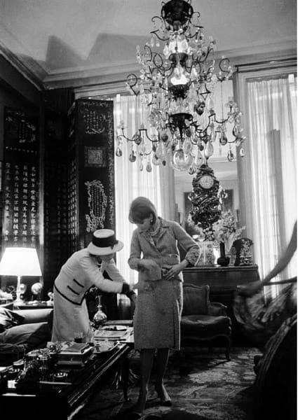 Black and white photograph of Coco Chanel making an adjustment on a model in her private apartment, House of Chanel