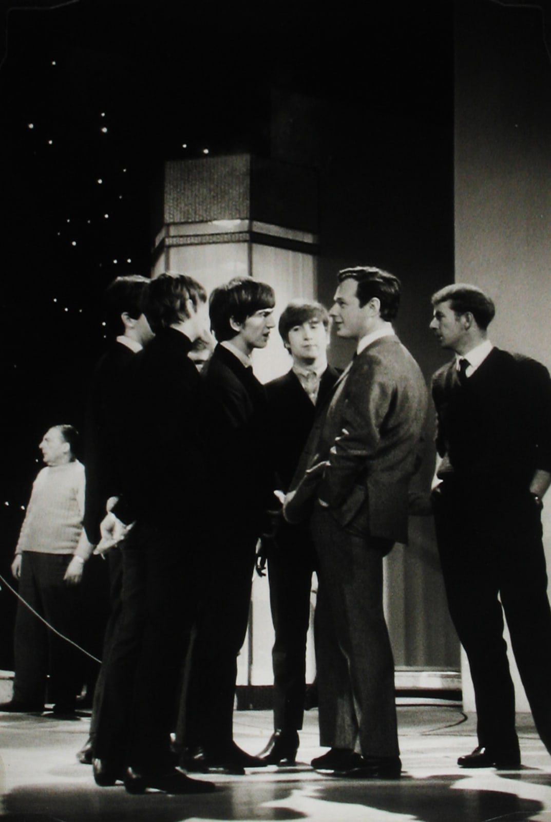 Black and white photograph of the Beatles speaking to their manager Brian Epstein, on set for the Ed Sullivan show.