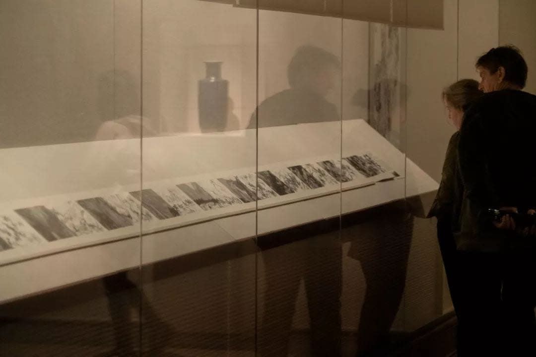 The album is unfolded and displayed in the museum's showcase, and there are two person look at it.
