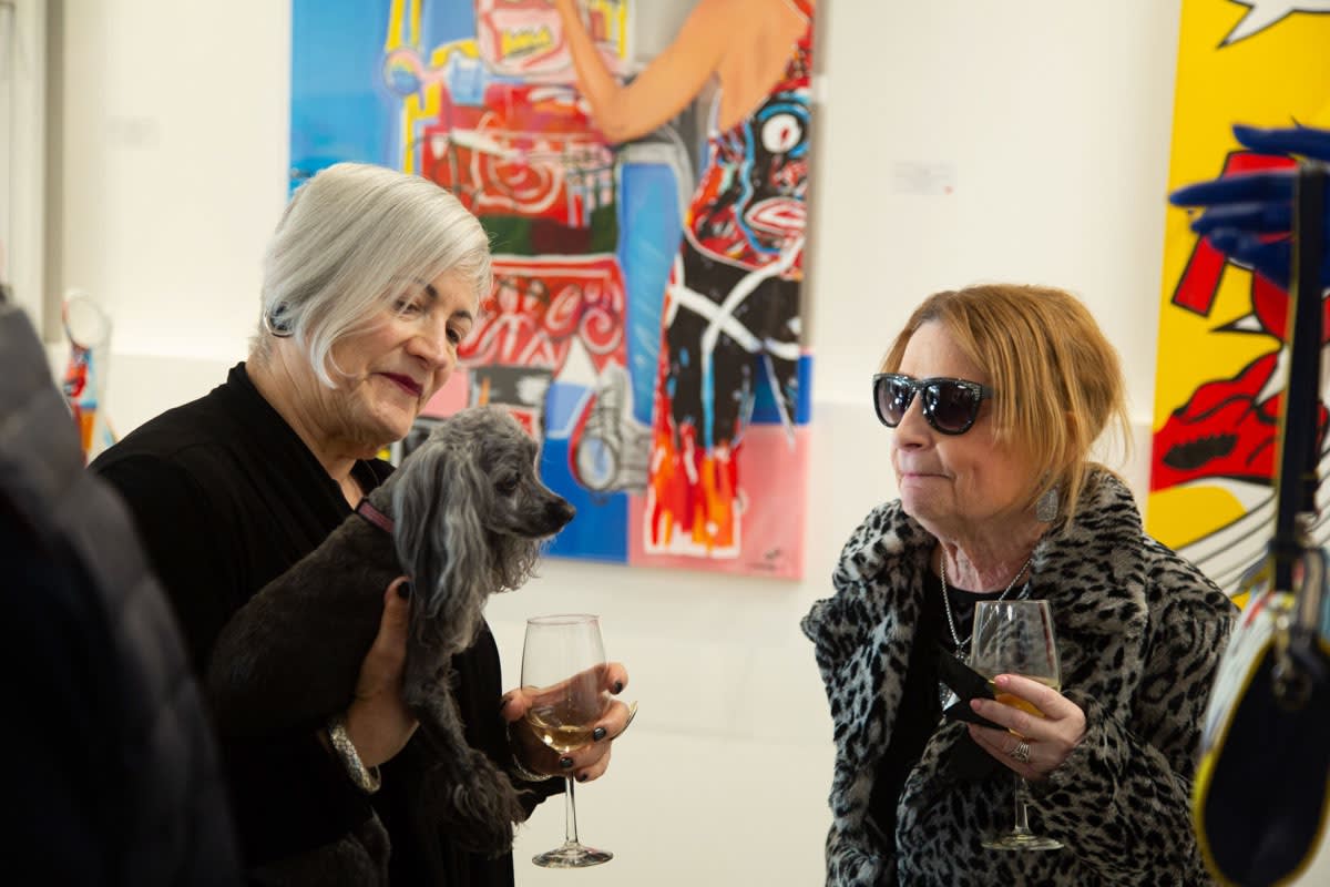Women with dog in front of paintings displayed at Carousel Fine Art's gallery space in Buckhead Village, Atlanta during the Caroline Dechamby Retrospective.