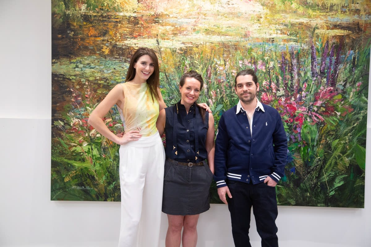 People posing in front of Eric Alfaro's paintings displayed in Carousel Fine Art's Buckhead Village location during the Eric Alfaro exhibition "Spring Reverie."
