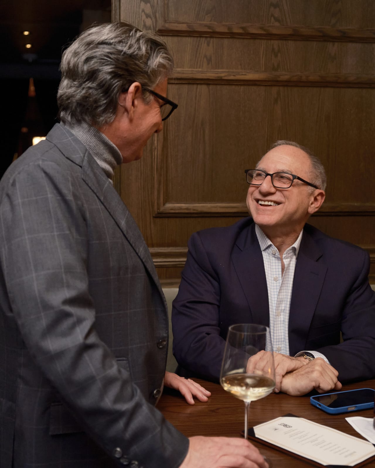 Networking cluster of agents and collectors enjoying drinks and conversation under large cityscape print.