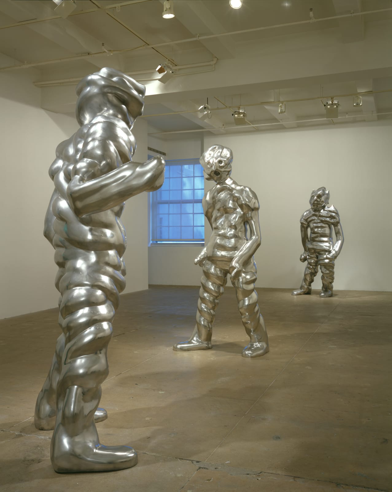installation image of three abstract sculptures of twisted metal resembling human-like figures