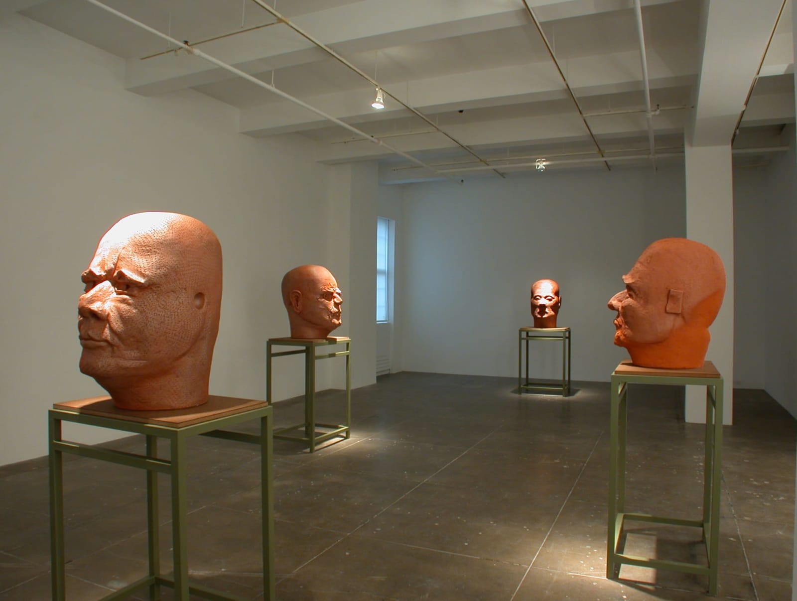 Large sculptures of bald heads of men on tables in a gallery room.