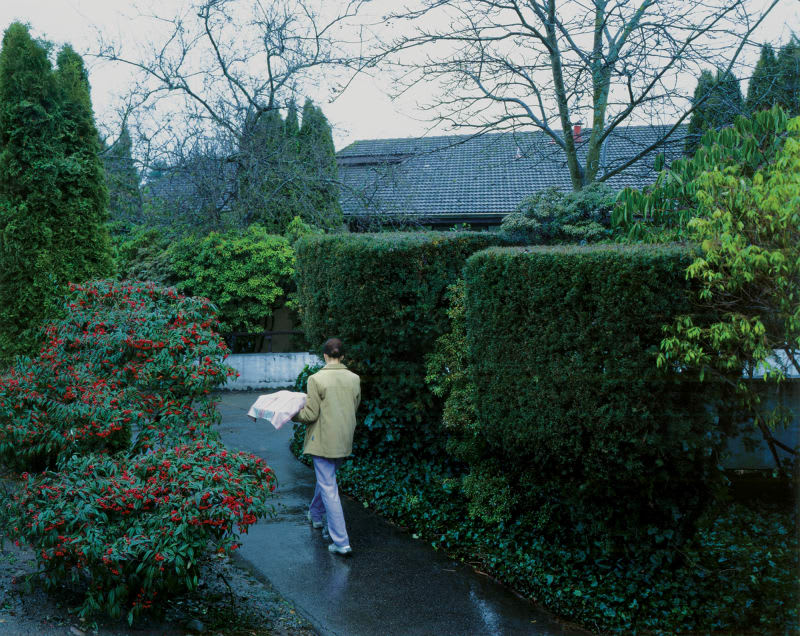 A woman holding a parcel walking on a damp day near homes and gardens.