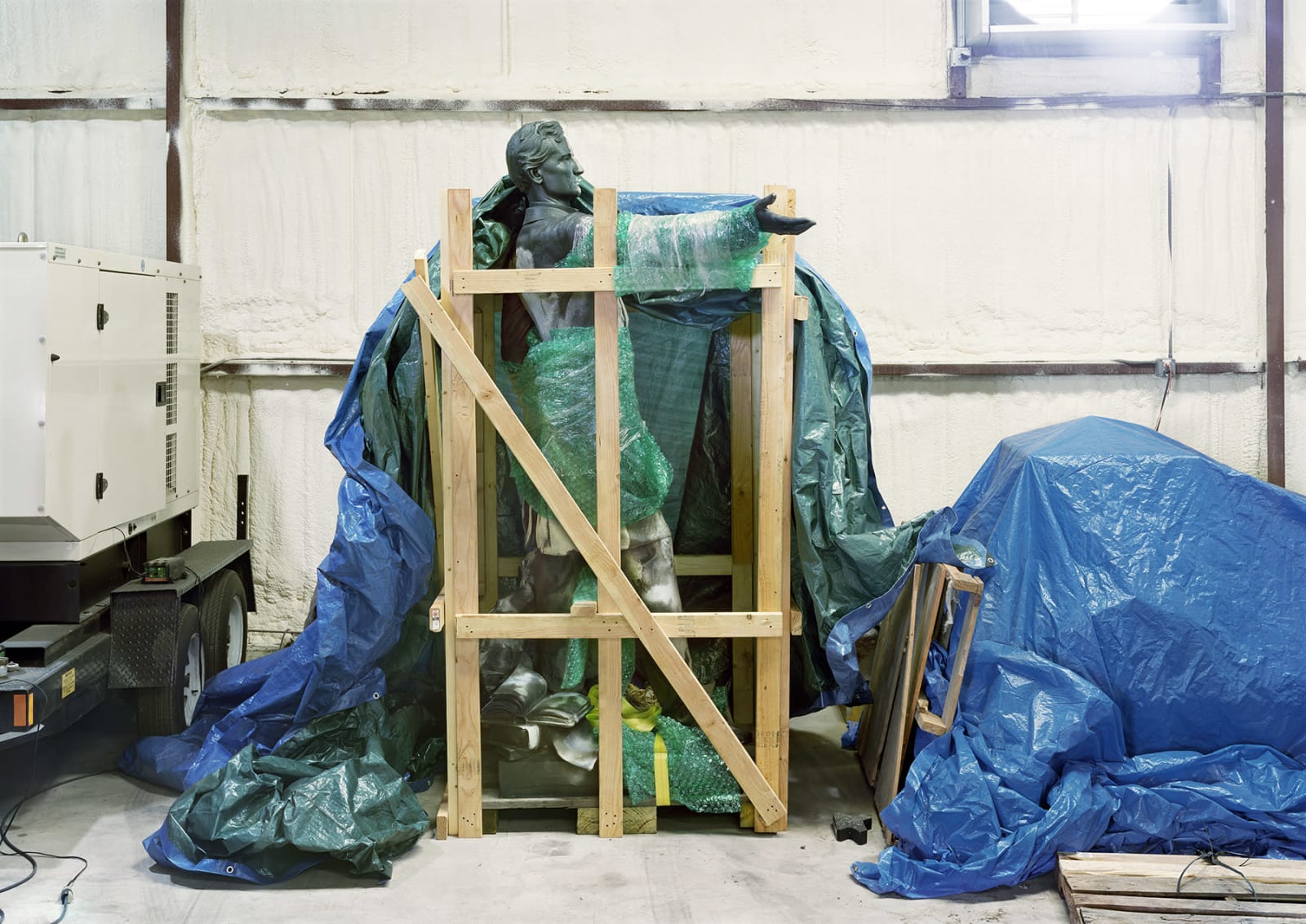 An image containing a removed monument wrapped in bubble wrap, as captured in a photography by An-My Lê