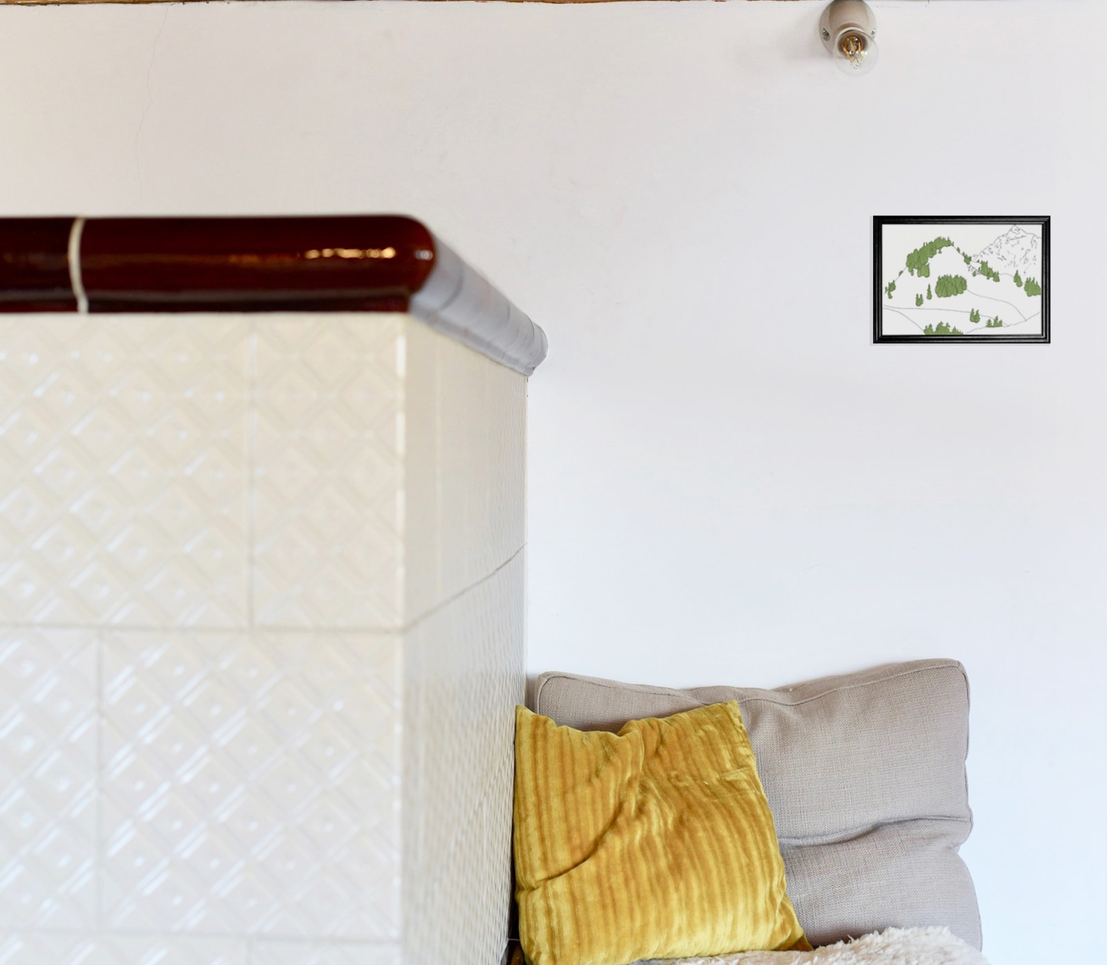 anna-stemmer-dworak-image is a mockup of a framed drawing of a snow covered mountain hanging over a seat with pillows and an old big white tile oven