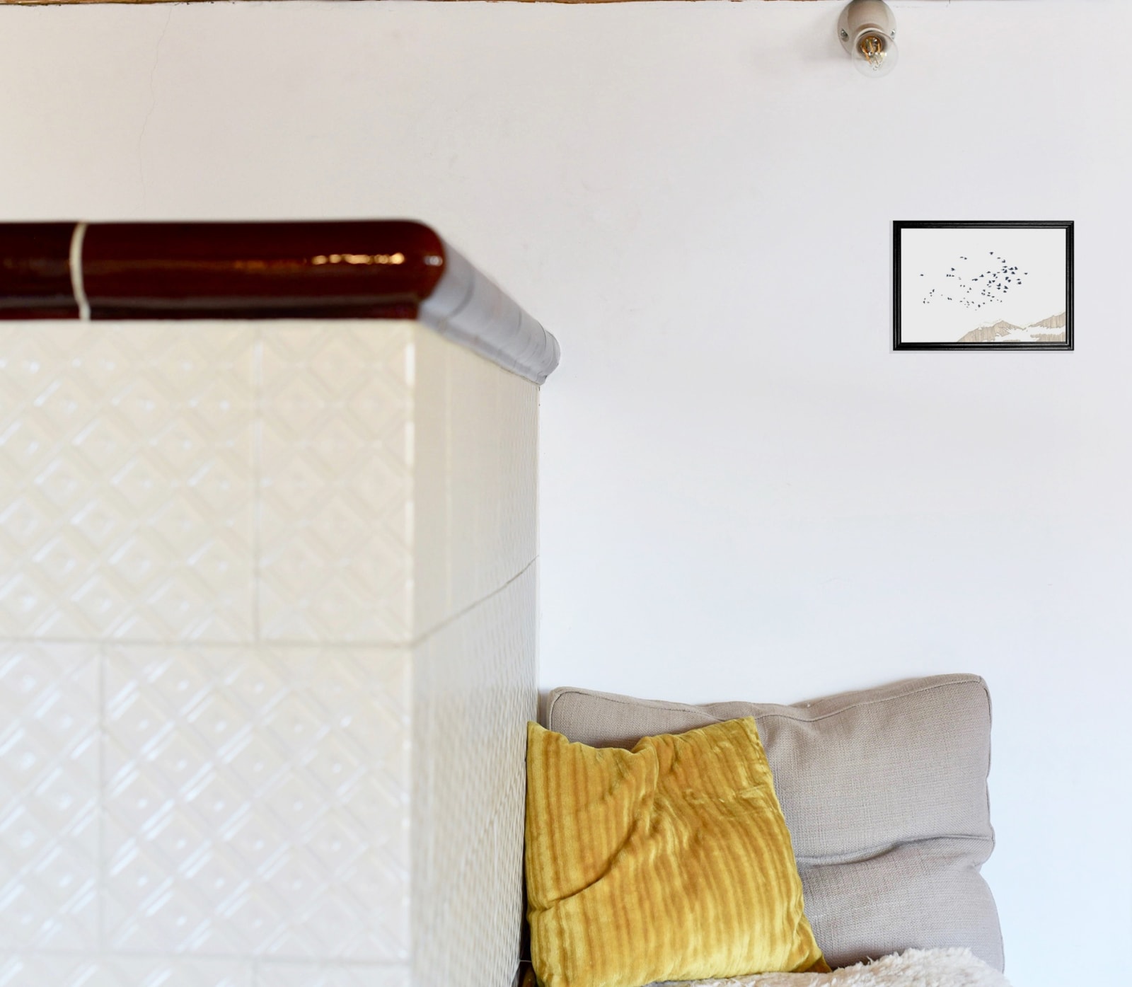 anna-stemmer-dworak-image is a mockup of a framed drawing of a flock of birds flying hanging over a seat with pillows and an old big white tile oven