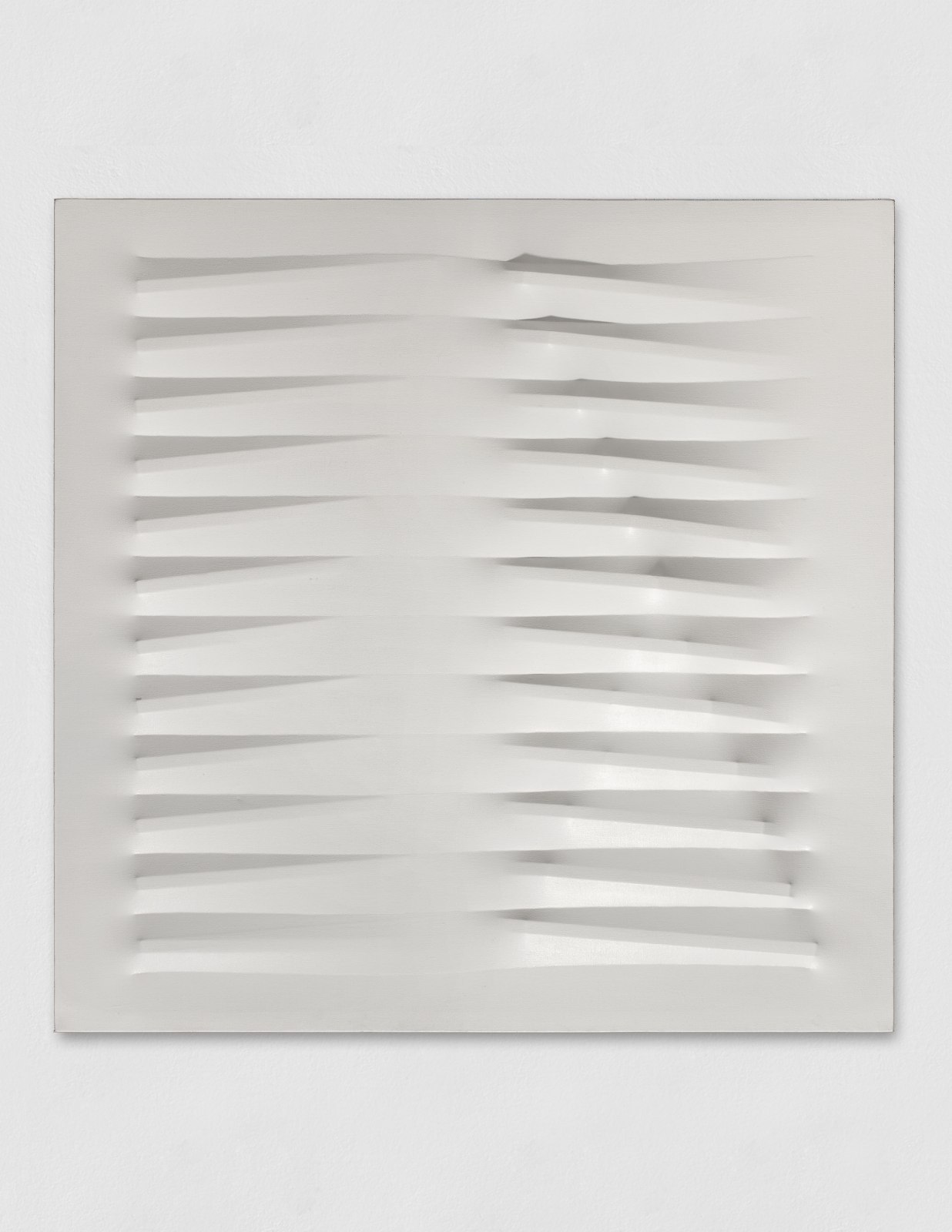 A white wall sculpture made with vinyl tempera laid over nails to create an undulating pattern.