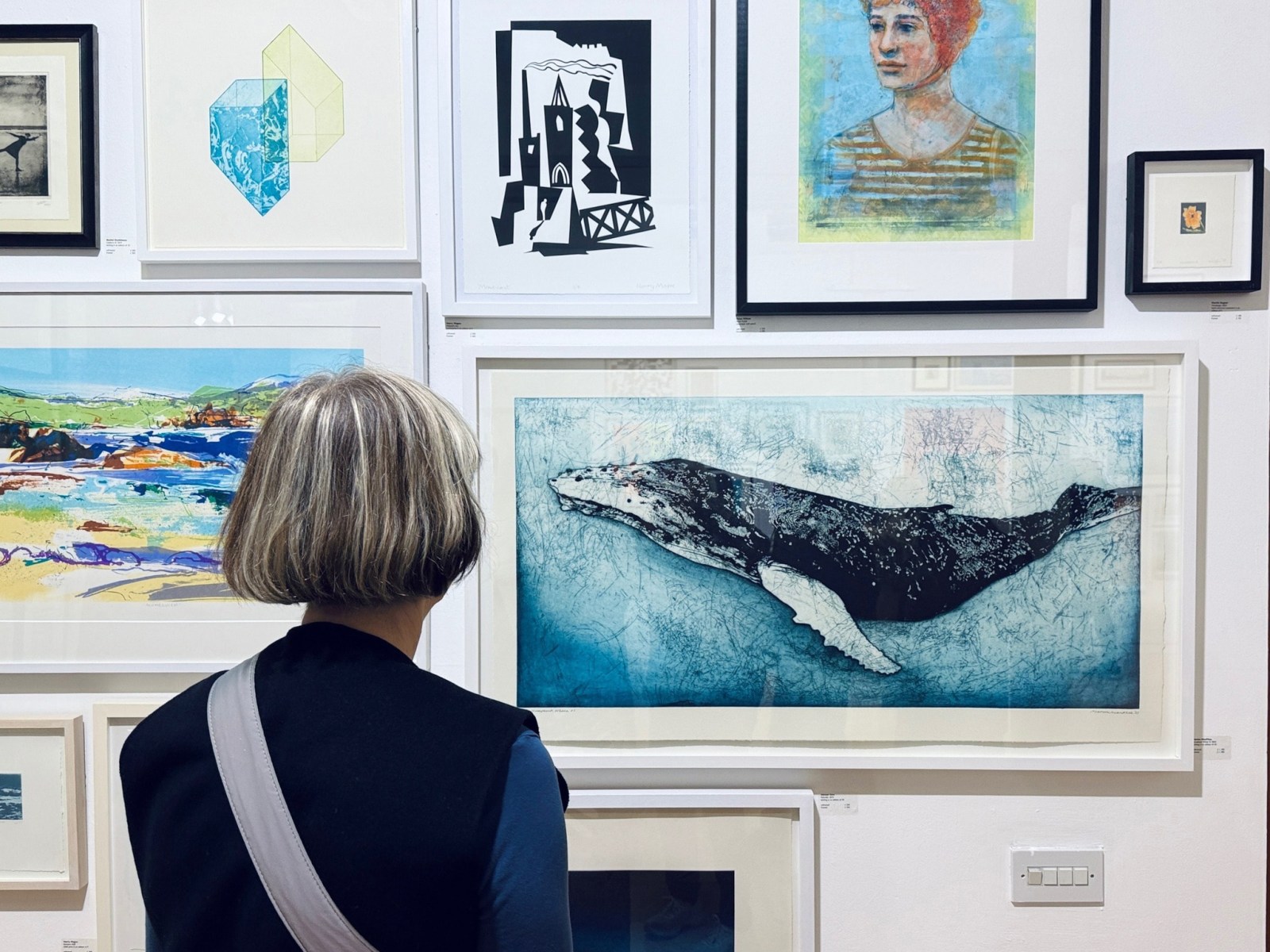 the back of a woman's head, she is looking at a wall covered in prints