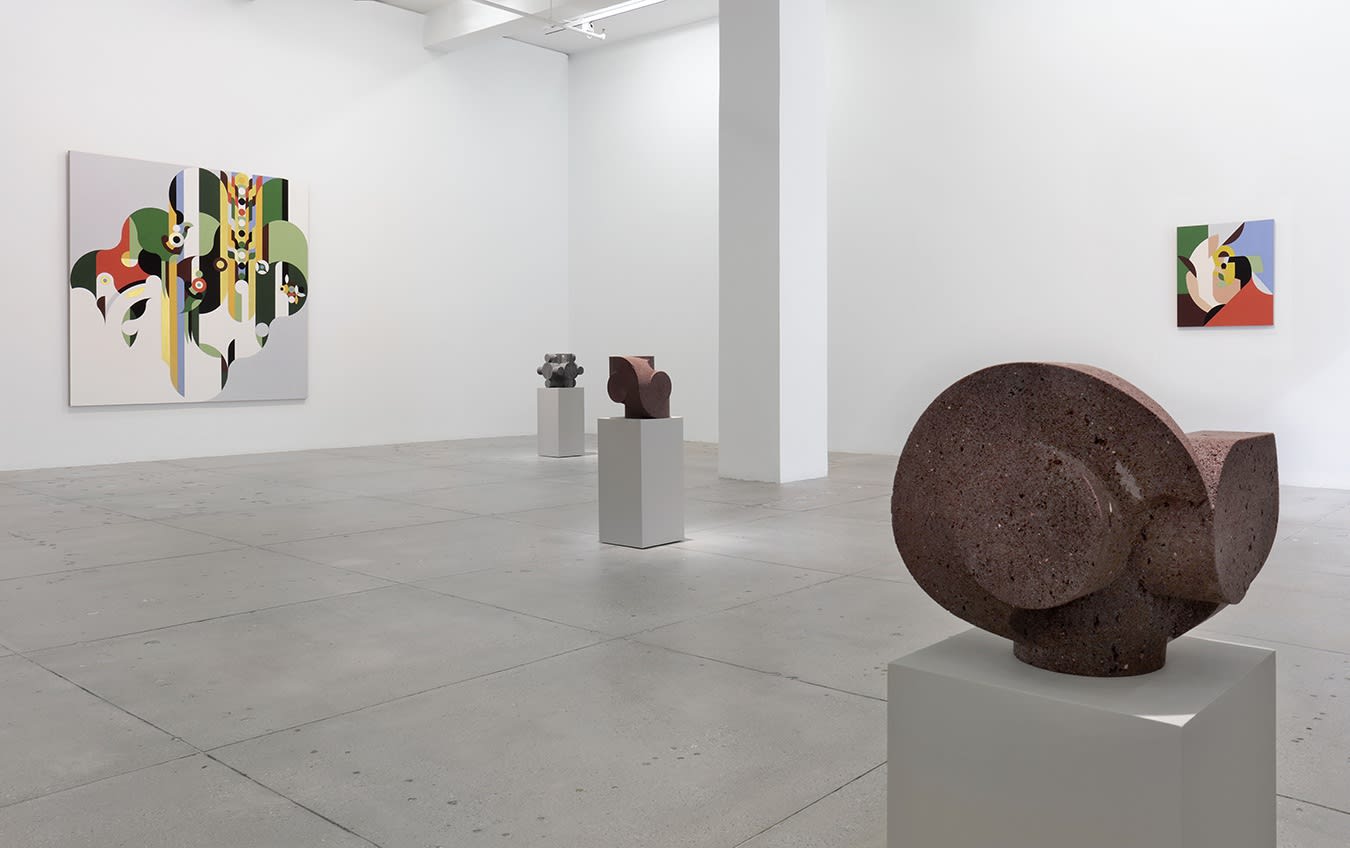 In a large white space, two abstract paintings hang on the wall behind 3 small, dark stone sculptures.