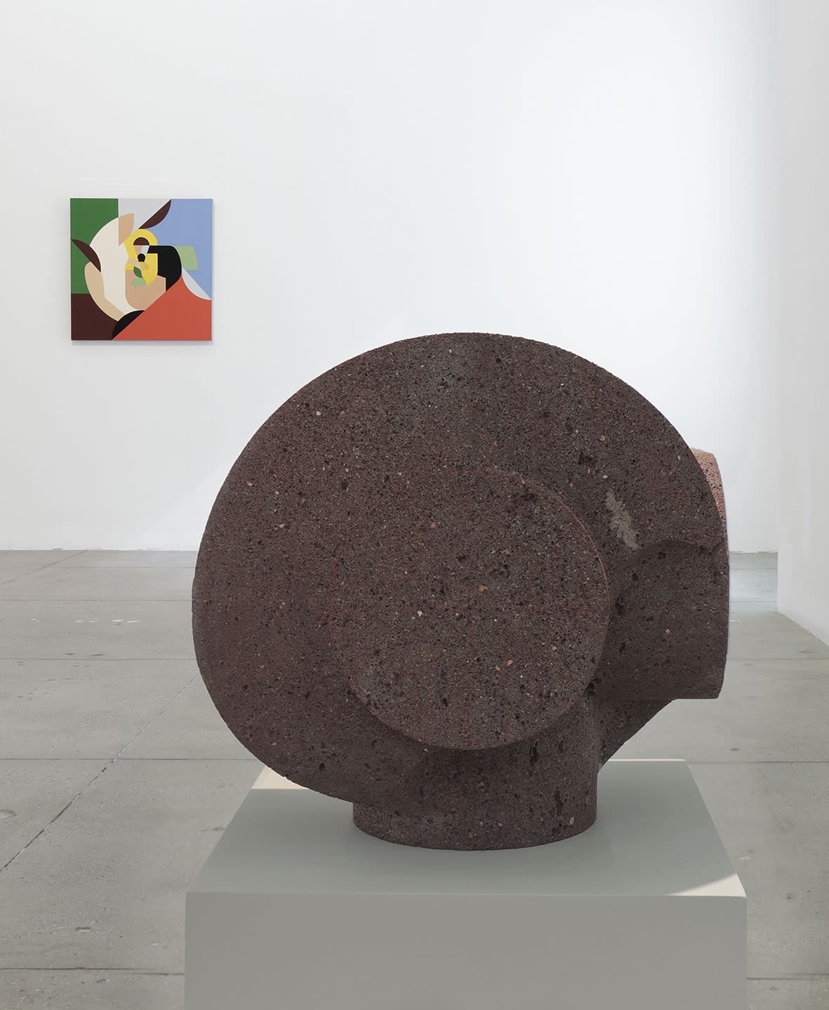 1 small stone sculpture stands to the left of a colorful abstract painting on a white wall.