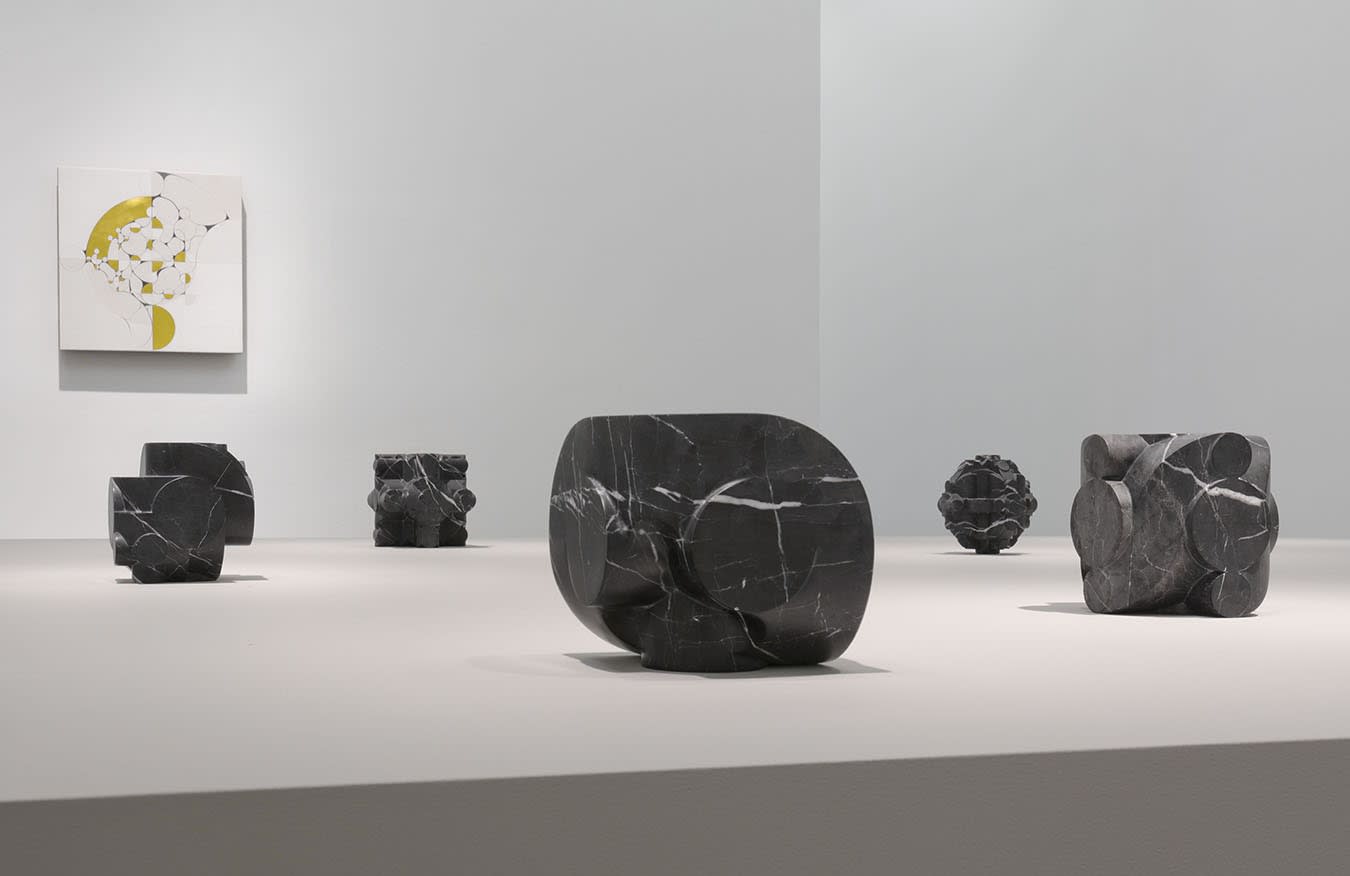 5 small stone sculptures in front of a colorful abstract painting on a white wall.