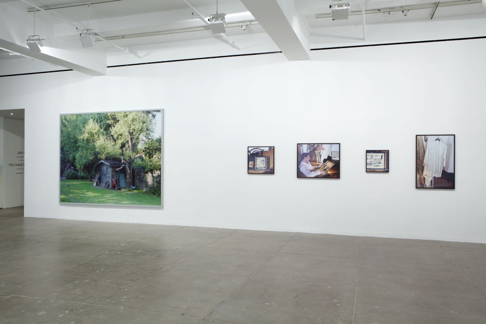 One large photograph of a treehouse hangs alongside four small images of clothes, a man reading and knick-knacks. 