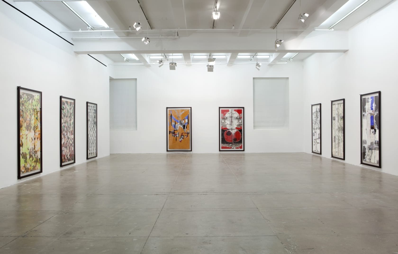 Eight large vertical abstract paintings fill the walls of a large white room. 