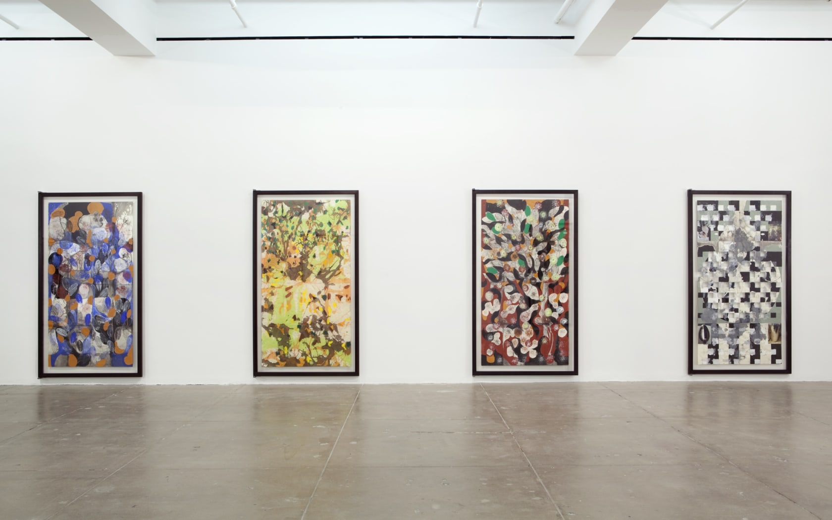 Four large vertical paintings with geometric shapes, flower-like patterns and monochromatic color schemes hang on a white wall. 