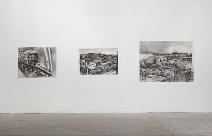 A white wall features three large charcoal drawings depicting urban and rural landscapes. 