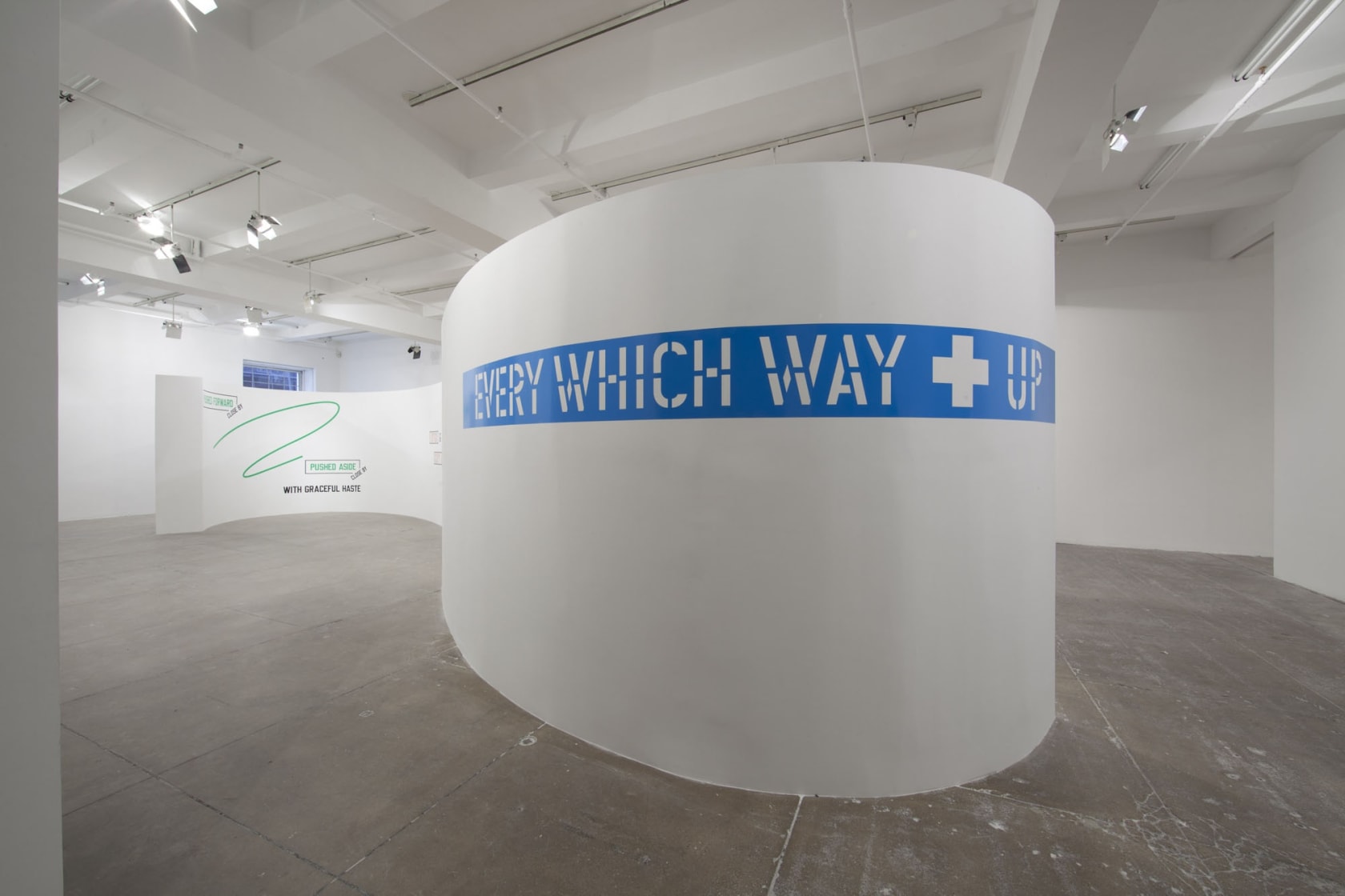 On a curved white wall, large white text over a blue background strip reads: EVERY WHICH WAY UP