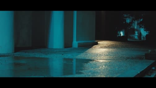 A wet sidewalk glistens at night under green light. 