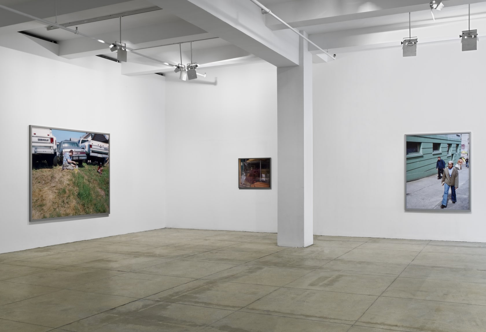 3 framed, color photographs of various sizes hang in the corner of a white room. There is a white column in the center. 