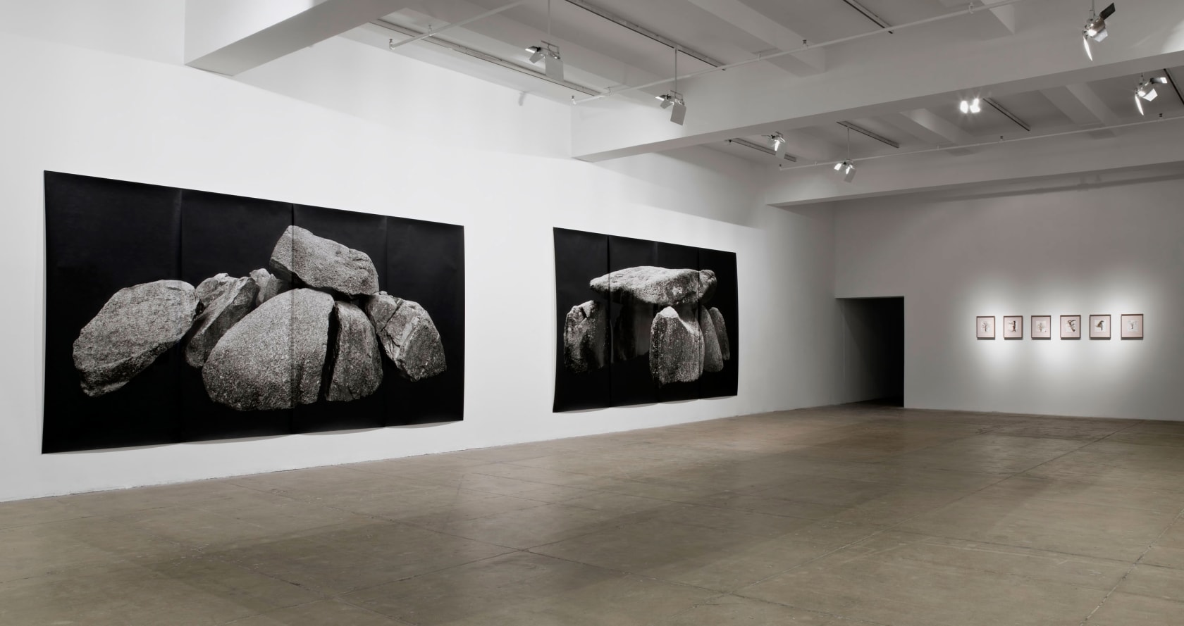 Two large prints of stacked rocks on a black background are pinned to the left wall. Six framed drawings of bare trees hang on the right wall. 