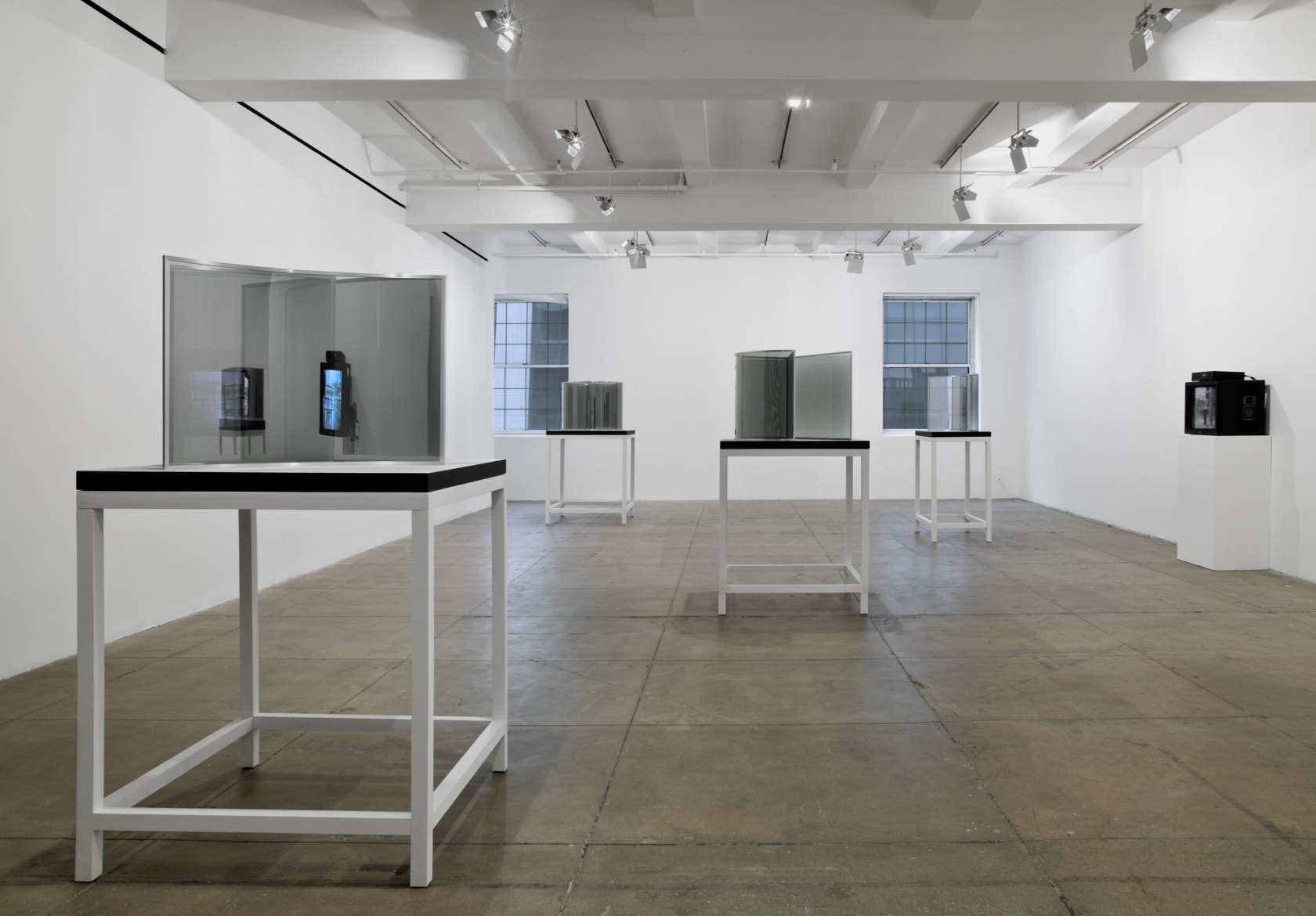 Four glass and mirror sculptures reflecting their surroundings are displayed atop wooden tables. 