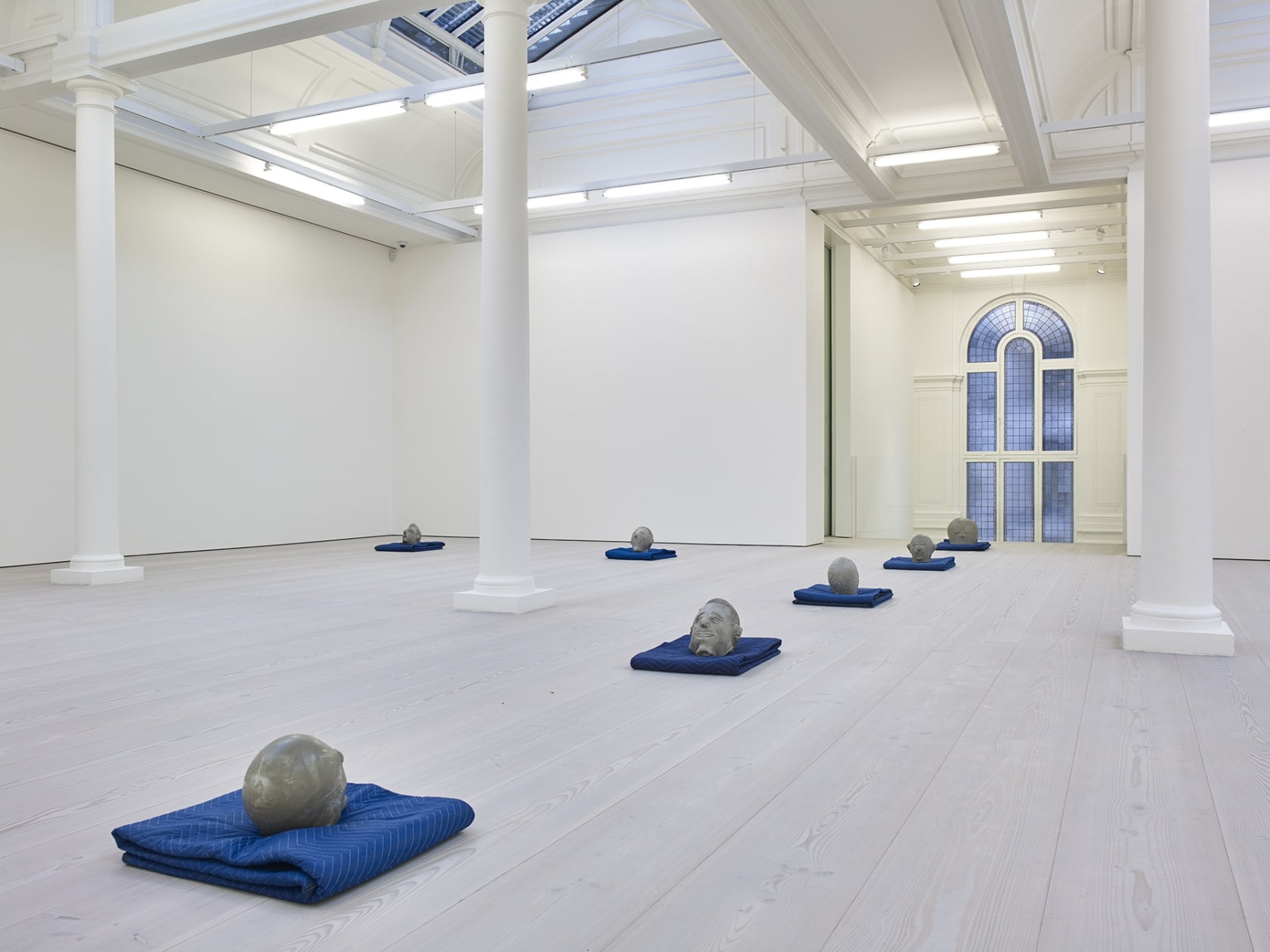 Gallery view, numerous abstract clay heads resting on blue blankets.