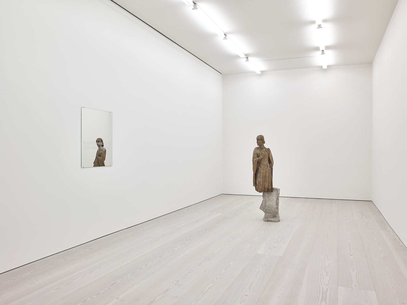 Figurative stone statue mounted on rock faces mirror on wall.