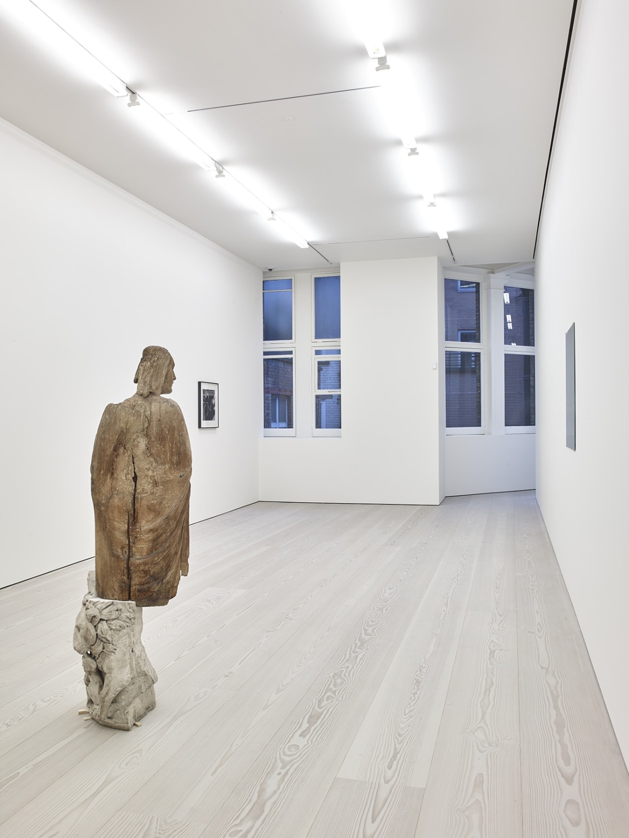 Brown figurative statue mounted on stone from behind.