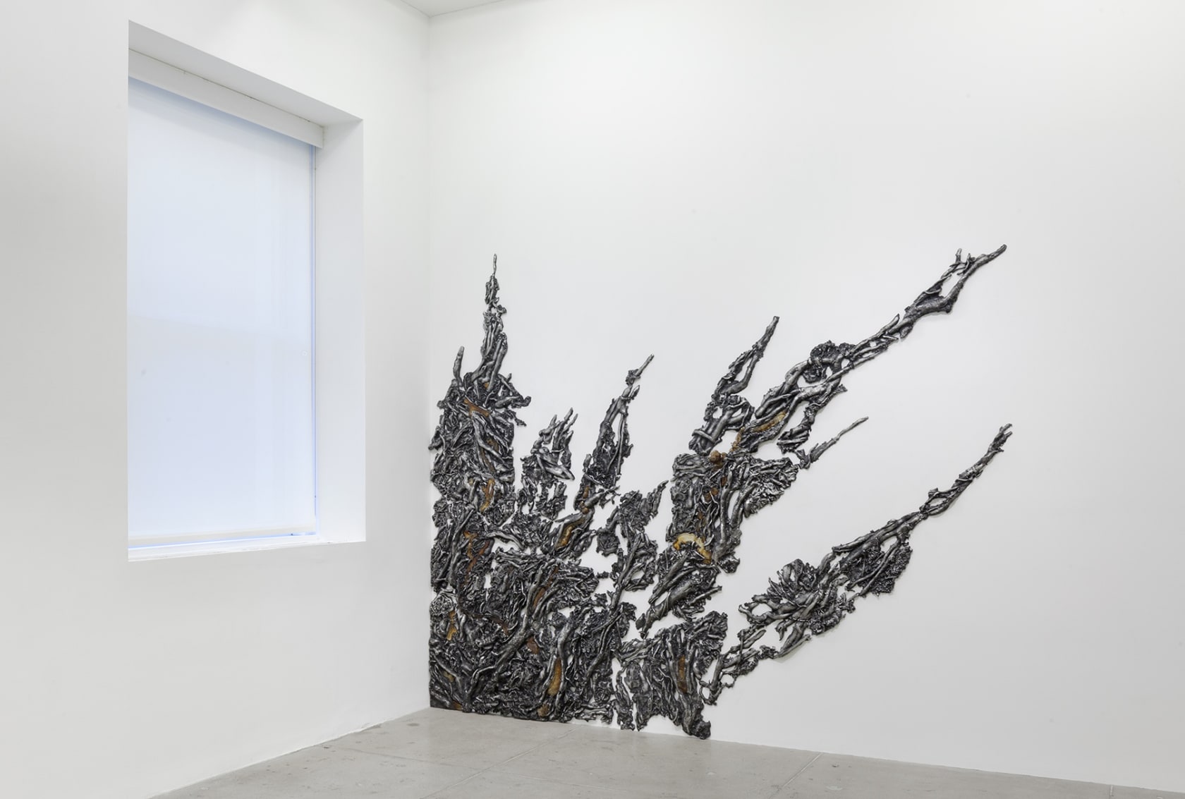 An organic, plant-like form climbs up the gallery wall from the floor next to a window.