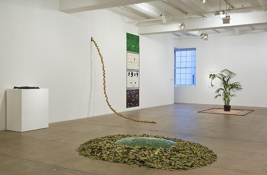 An installation view of various sculptures made of plants and leaves and artworks on a white wall. 