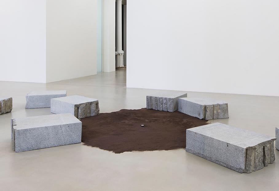 Installation of carved stone blocks around brown suede rug.