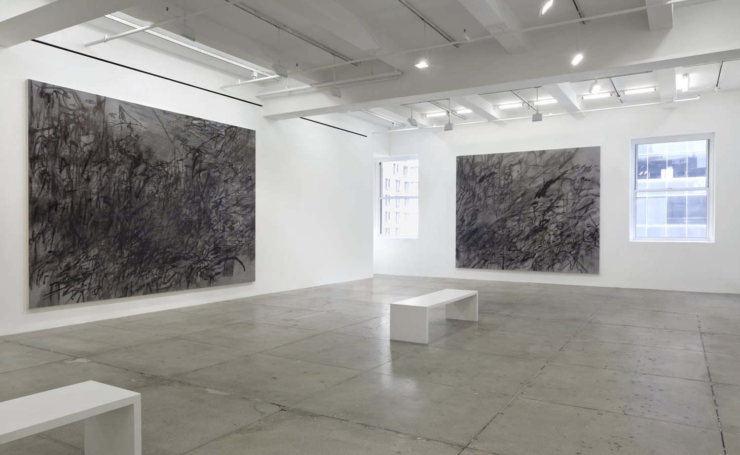 2 abstract paintings hang in a white gallery space with a bench.