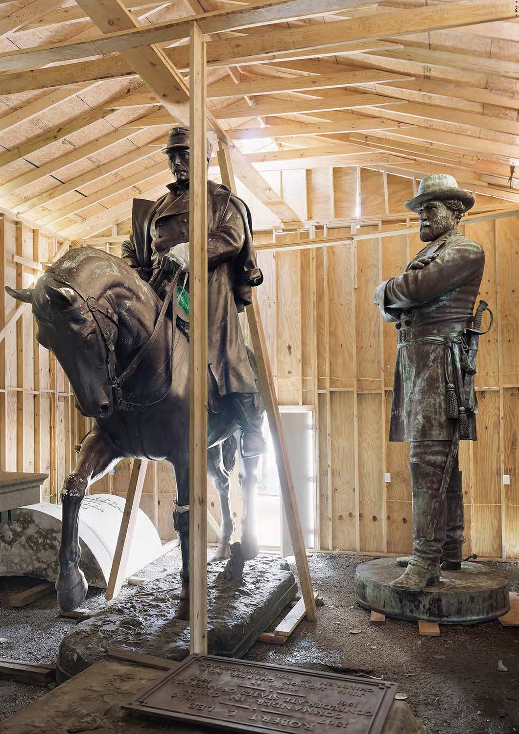 Two statues, one of a man and a man on a horse, stand within a plywood shed.
