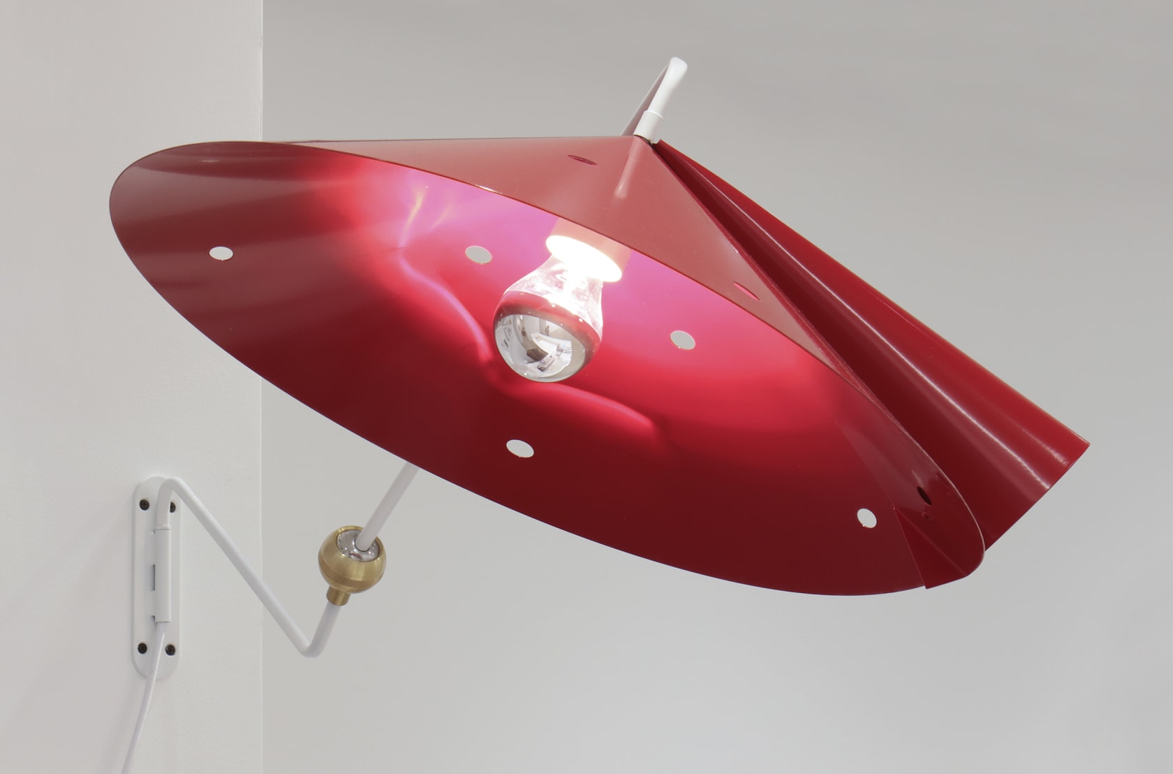 A red lampshade with a glowing lightbulb attached to the wall