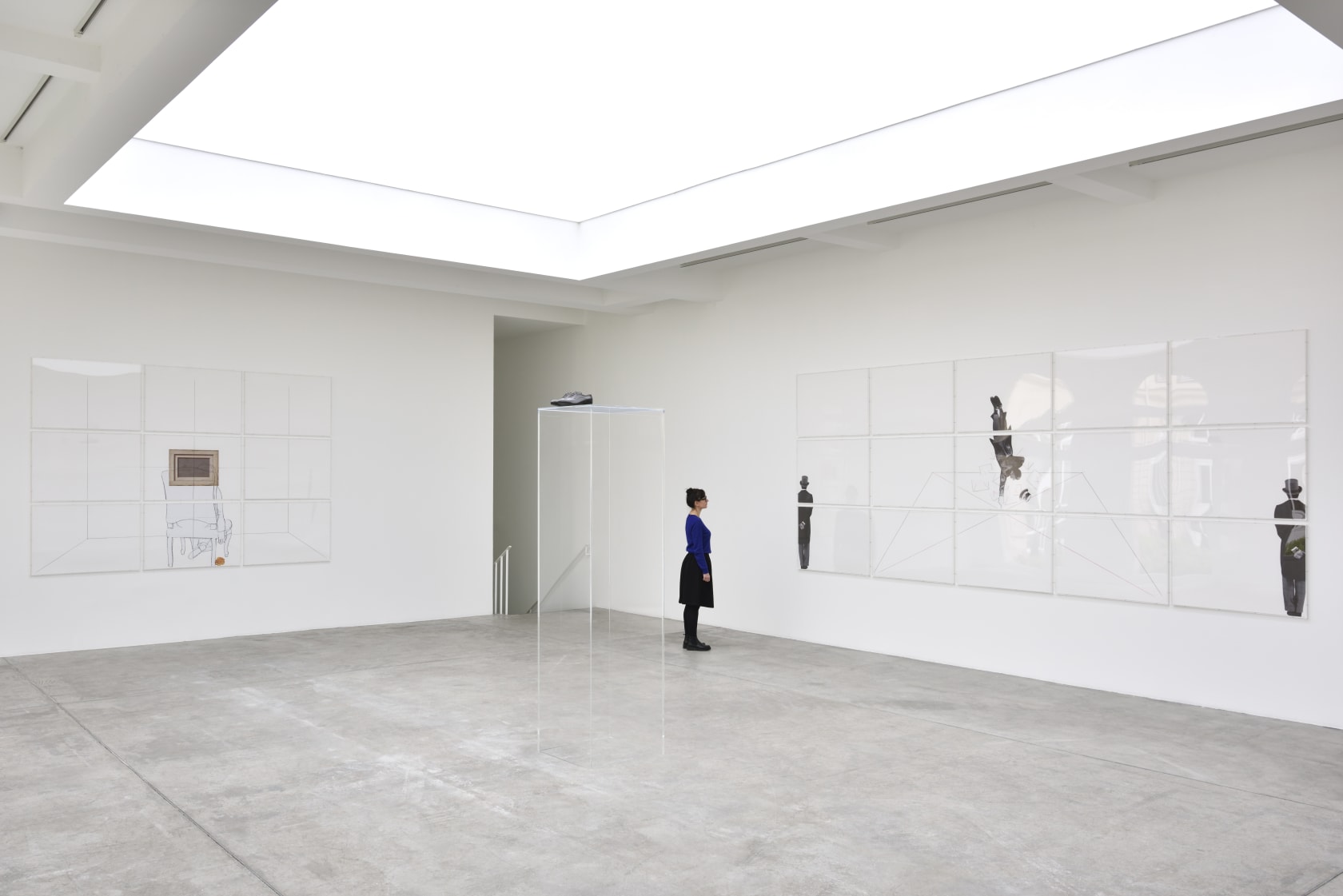 A woman looks at an artwork on the wall, there are various panels displaying a man with a hat.