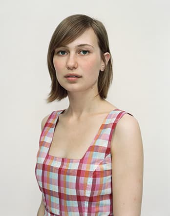 A Rineke Dijkstra portrait of a woman in a pink and red plaid shirt.