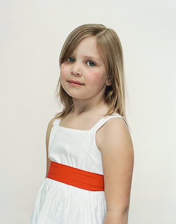 A Rineke Dijkstra portrait of a young girl in a white dress with a red belt.