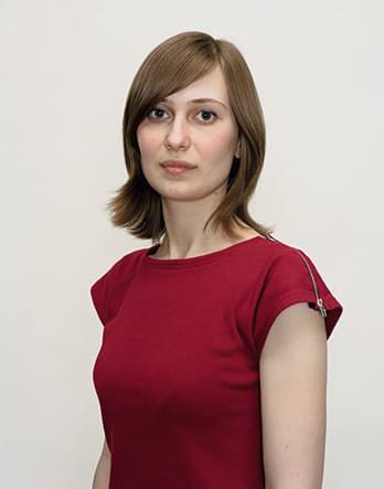 A Rineke Dijkstra portrait of a woman in a red shirt with short hair.