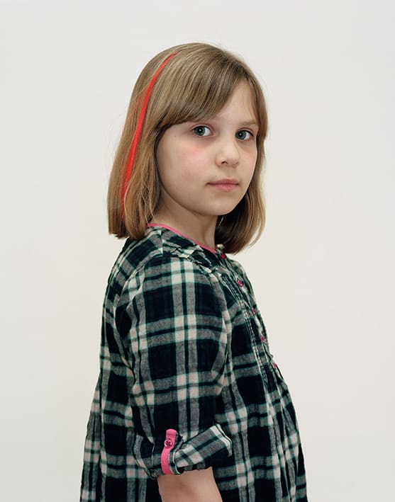 A Rineke Dijkstra portrait of a girl in a green plaid shirt with a red streak in her hair.