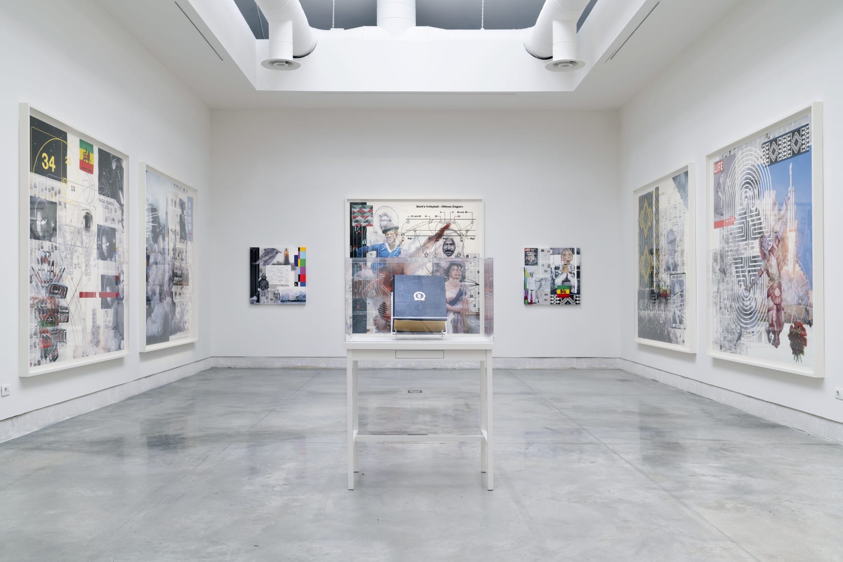 Installation view of an exhibition by Tavares Strachan with large framed works on the wall and a vitrine in the center of the room