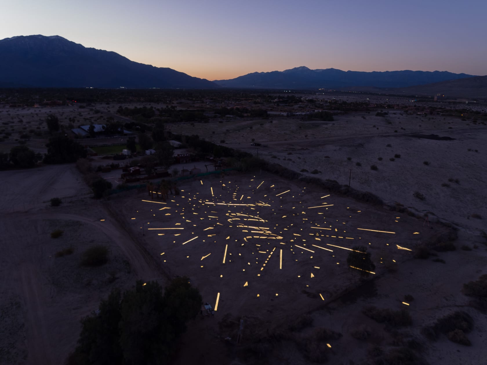 An outdoor neon installation by Tavares Strachan on the desert floor, photographed at sunset
