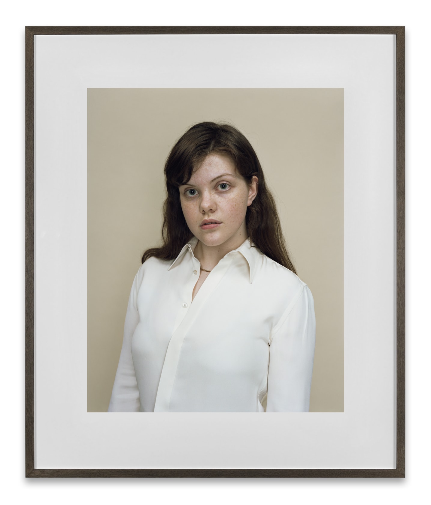 A Rineke Dijkstra portrait of the actress Georgie Henley in a white button down shirt in front of a neutral background. 