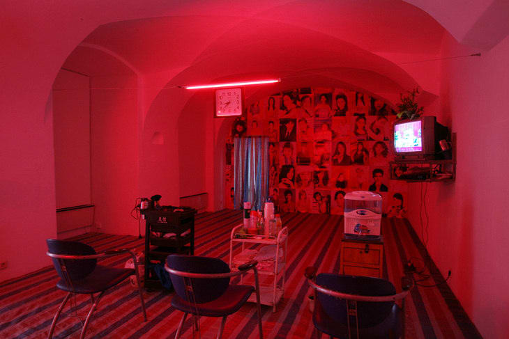 A barber shop is relocated into a room with pinkish lights and there's an old-fashioned TV hanging on the right wall in 2006.