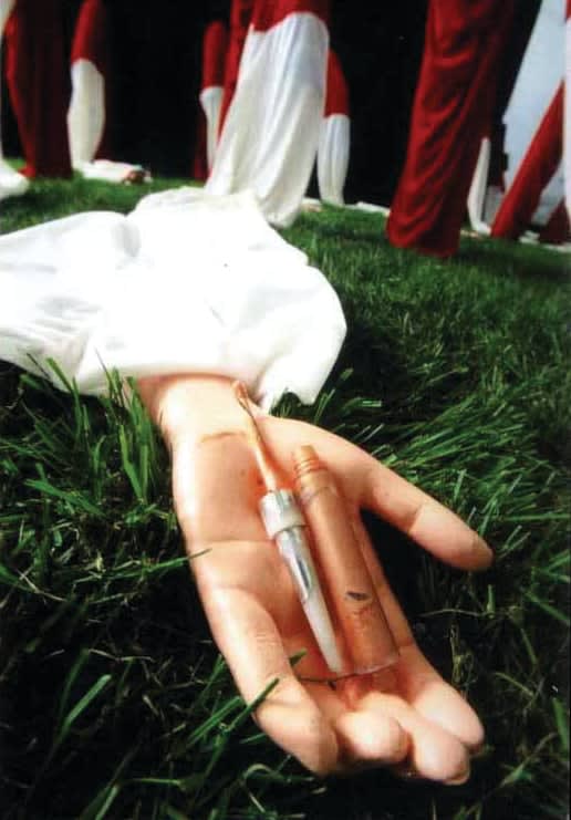 A closer shot of one of red-and-white long sleeves; a needle for injections is placed on the center of the palm of the artificial arm.