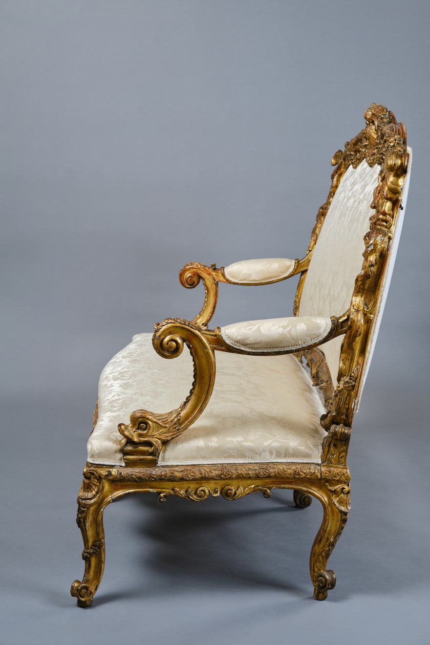 CARVED AND GILDED WOOD SOFA, FRANCE, 18th CENTURY, two-seater, mixtilinear layout and entirely traversed by relief carvings, with floral festoons, garlands, manly masks in the back uprights and stylized dolphins in the armrests with curly finials, upholstered in modern fabric with classical decoration, the back removable