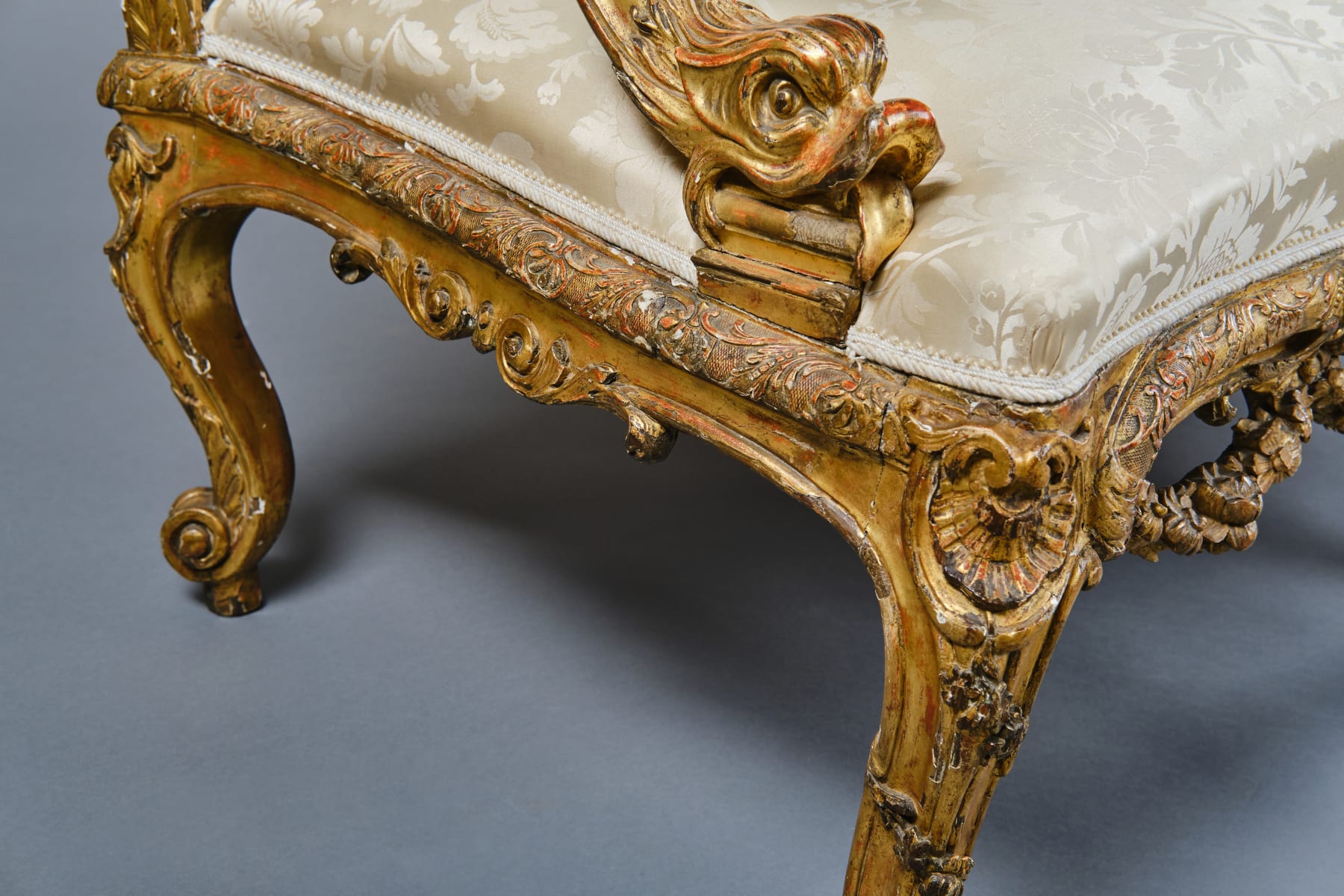 CARVED AND GILDED WOOD SOFA, FRANCE, 18th CENTURY, two-seater, mixtilinear layout and entirely traversed by relief carvings, with floral festoons, garlands, manly masks in the back uprights and stylized dolphins in the armrests with curly finials, upholstered in modern fabric with classical decoration, the back removable