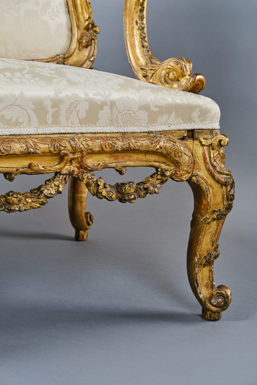 CARVED AND GILDED WOOD SOFA, FRANCE, 18th CENTURY, two-seater, mixtilinear layout and entirely traversed by relief carvings, with floral festoons, garlands, manly masks in the back uprights and stylized dolphins in the armrests with curly finials, upholstered in modern fabric with classical decoration, the back removable