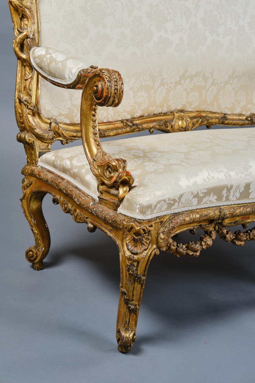 CARVED AND GILDED WOOD SOFA, FRANCE, 18th CENTURY, two-seater, mixtilinear layout and entirely traversed by relief carvings, with floral festoons, garlands, manly masks in the back uprights and stylized dolphins in the armrests with curly finials, upholstered in modern fabric with classical decoration, the back removable