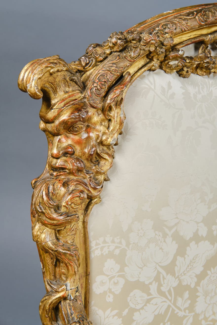 CARVED AND GILDED WOOD SOFA, FRANCE, 18th CENTURY, two-seater, mixtilinear layout and entirely traversed by relief carvings, with floral festoons, garlands, manly masks in the back uprights and stylized dolphins in the armrests with curly finials, upholstered in modern fabric with classical decoration, the back removable